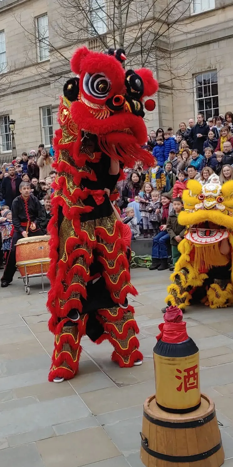 A red lion performing beside a wine barrel in front of a crowd